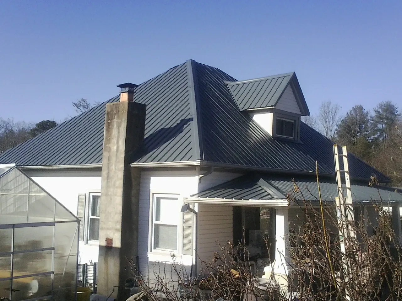 Dark blue standing seam metal roof on a white farmhouse with dormer — Slate & Tile Roof Repair by Roofing Brothers in Crittenden