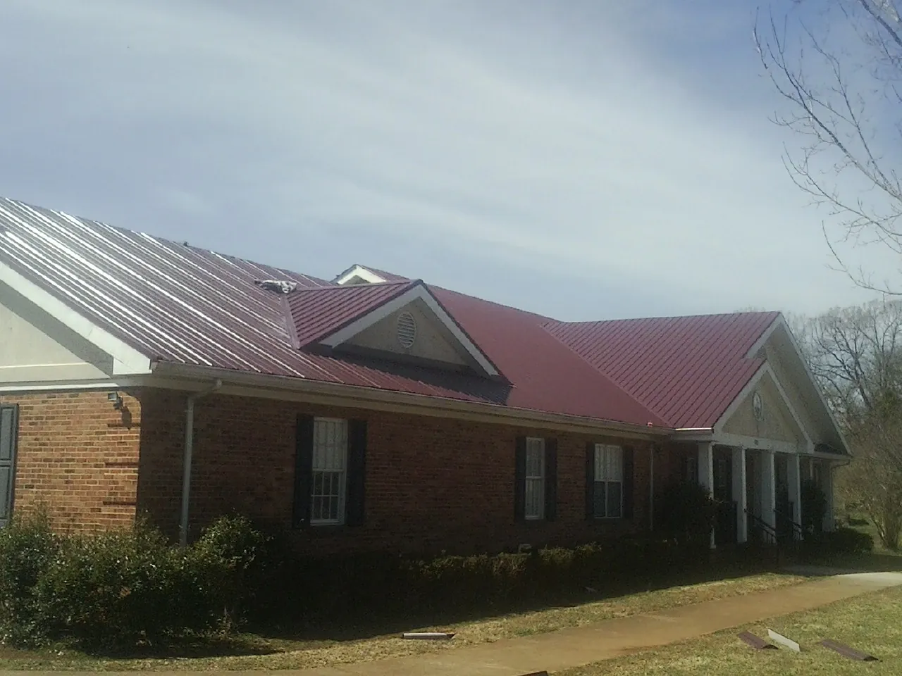 Red metal roof with gabled entries on a long brick building, from a Hail Damage Roof Repair job in Crittenden