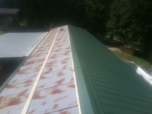 Old rusted panels beside newly installed green metal roofing — Wind Damage Roof Repair by Roofing Brothers in Crittenden
