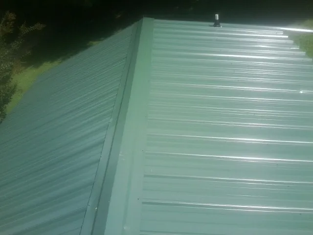 New green metal panels meeting at the ridge of a roof — Flat Roof Repair work by our crew in Crittenden