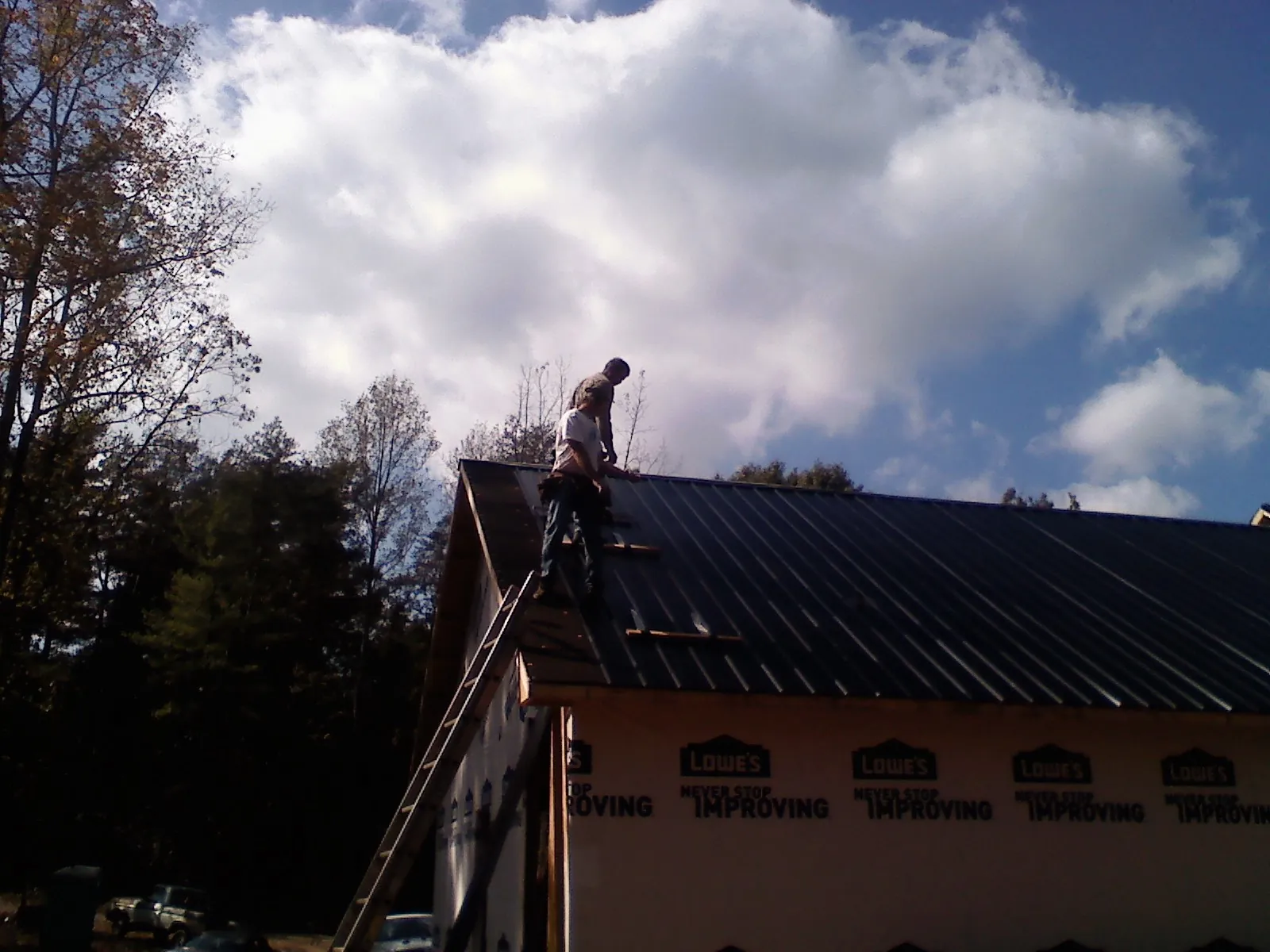 Roofer fastening dark metal panels high against a cloudy sky, from a Roof Inspection job in Crittenden