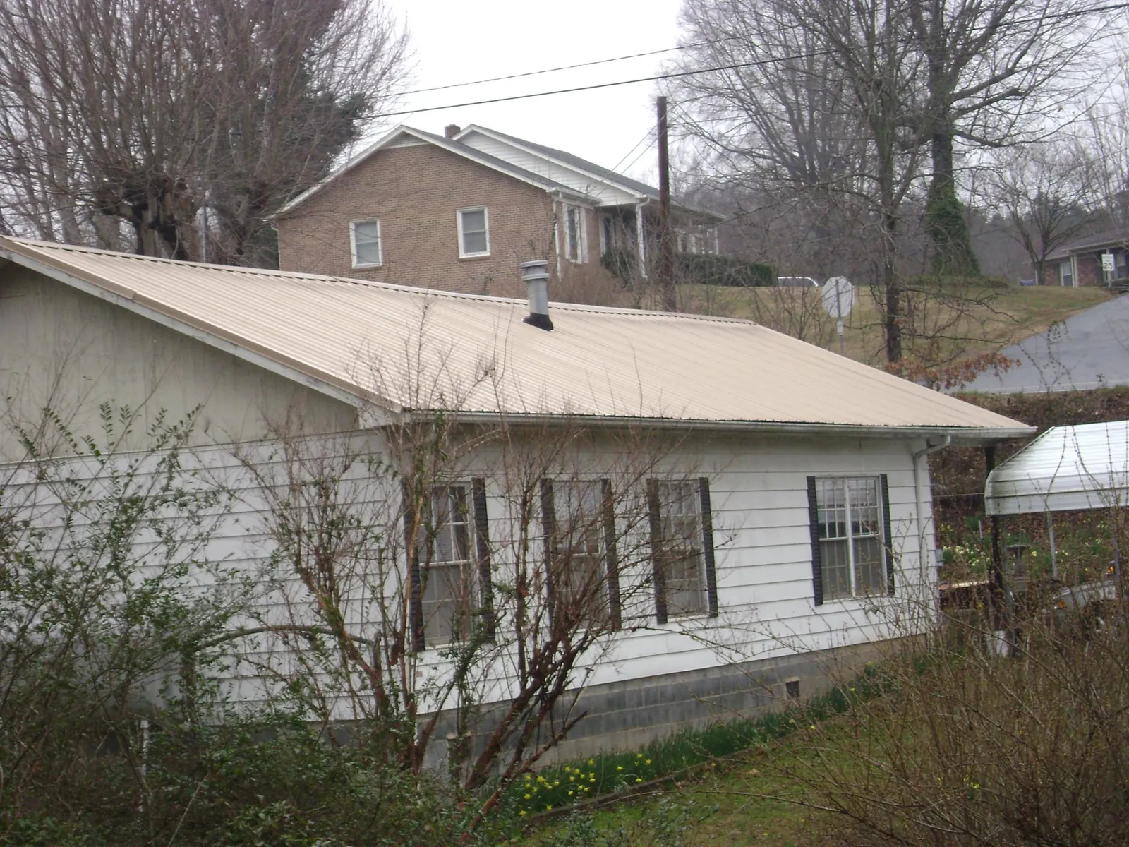 Tan metal roof on a white sided house set into a hillside — Commercial Roofing by Roofing Brothers in Crittenden