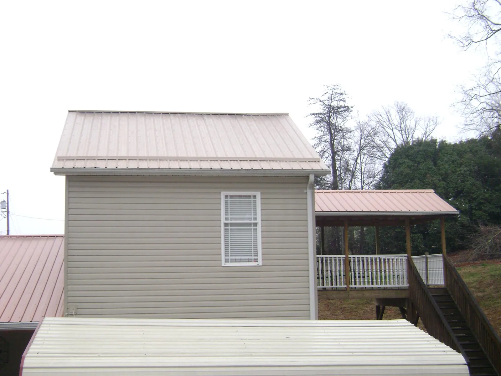 Tan metal roofs on a two story addition and attached porch, from a Roof Replacement job in Crittenden